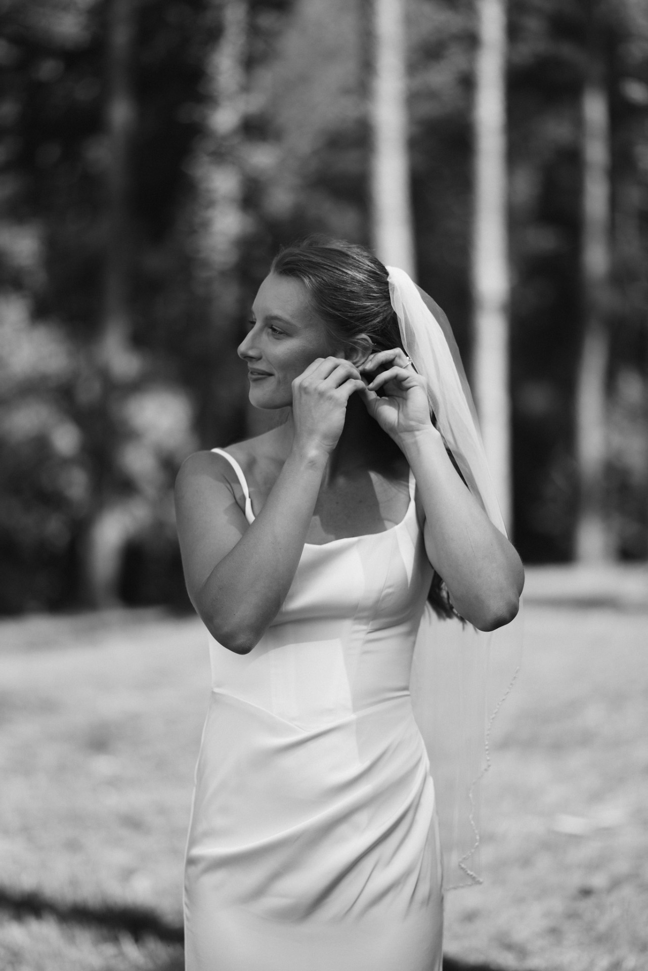 Black and white bridal portrait as the bride adjusts her earring outdoors